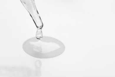 Photo of Glass pipette and transparent liquid on white background, closeup. Space for text