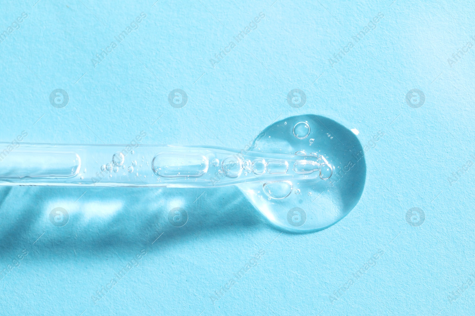 Photo of Glass pipette and transparent liquid on light blue background, top view