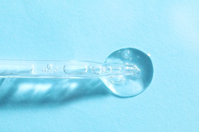 Glass pipette and transparent liquid on light blue background, top view