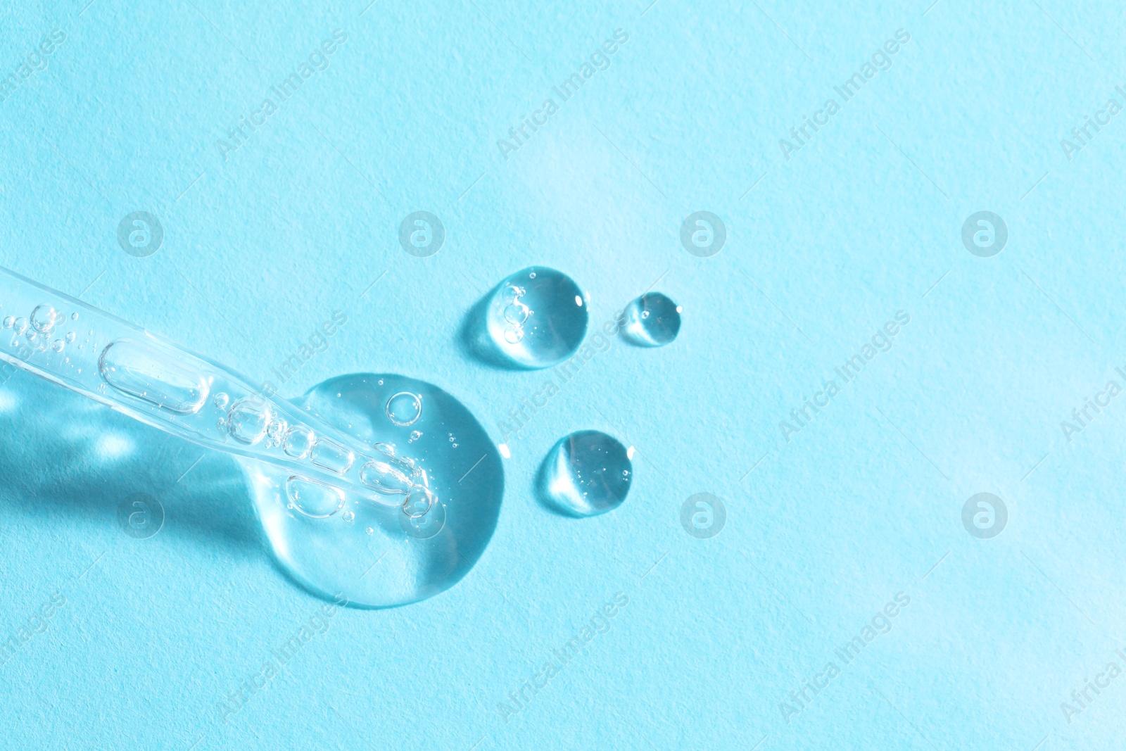 Photo of Glass pipette and transparent liquid on light blue background, top view. Space for text