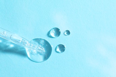 Glass pipette and transparent liquid on light blue background, top view. Space for text