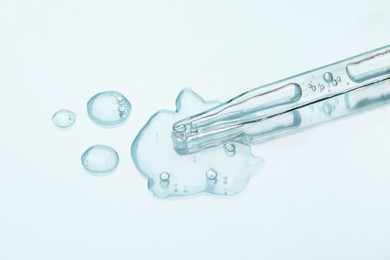 Photo of Glass pipette and transparent liquid on light background, closeup
