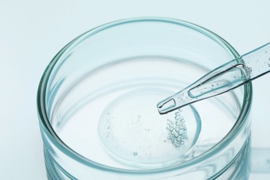Glass pipette and petri dish with liquid on light background, closeup