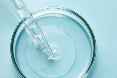 Photo of Glass pipette and petri dish with liquid on light blue background, top view