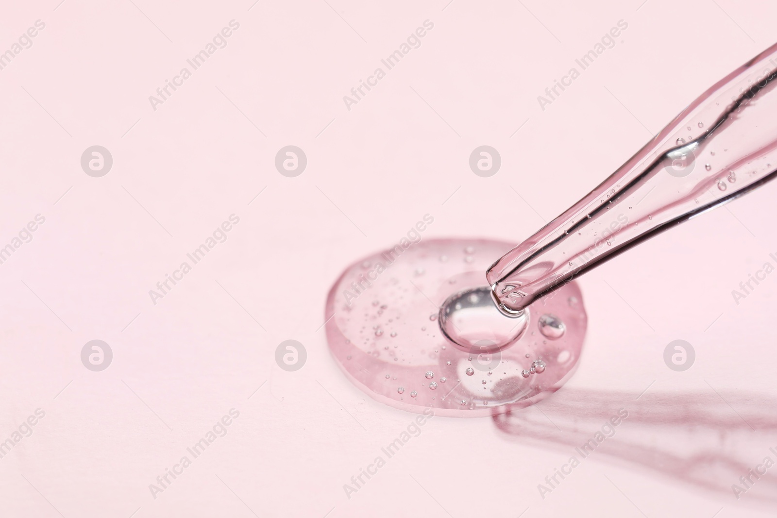 Photo of Glass pipette and transparent liquid on light pink background, closeup. Space for text