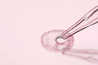 Glass pipette and transparent liquid on light pink background, closeup. Space for text