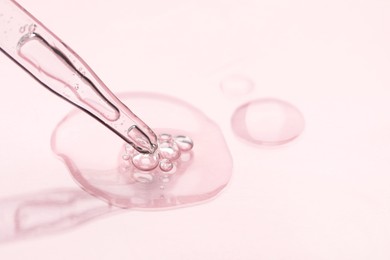 Photo of Glass pipette and transparent liquid on light pink background, closeup