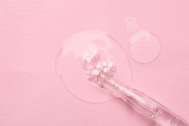 Glass pipette and transparent liquid on light pink background, top view