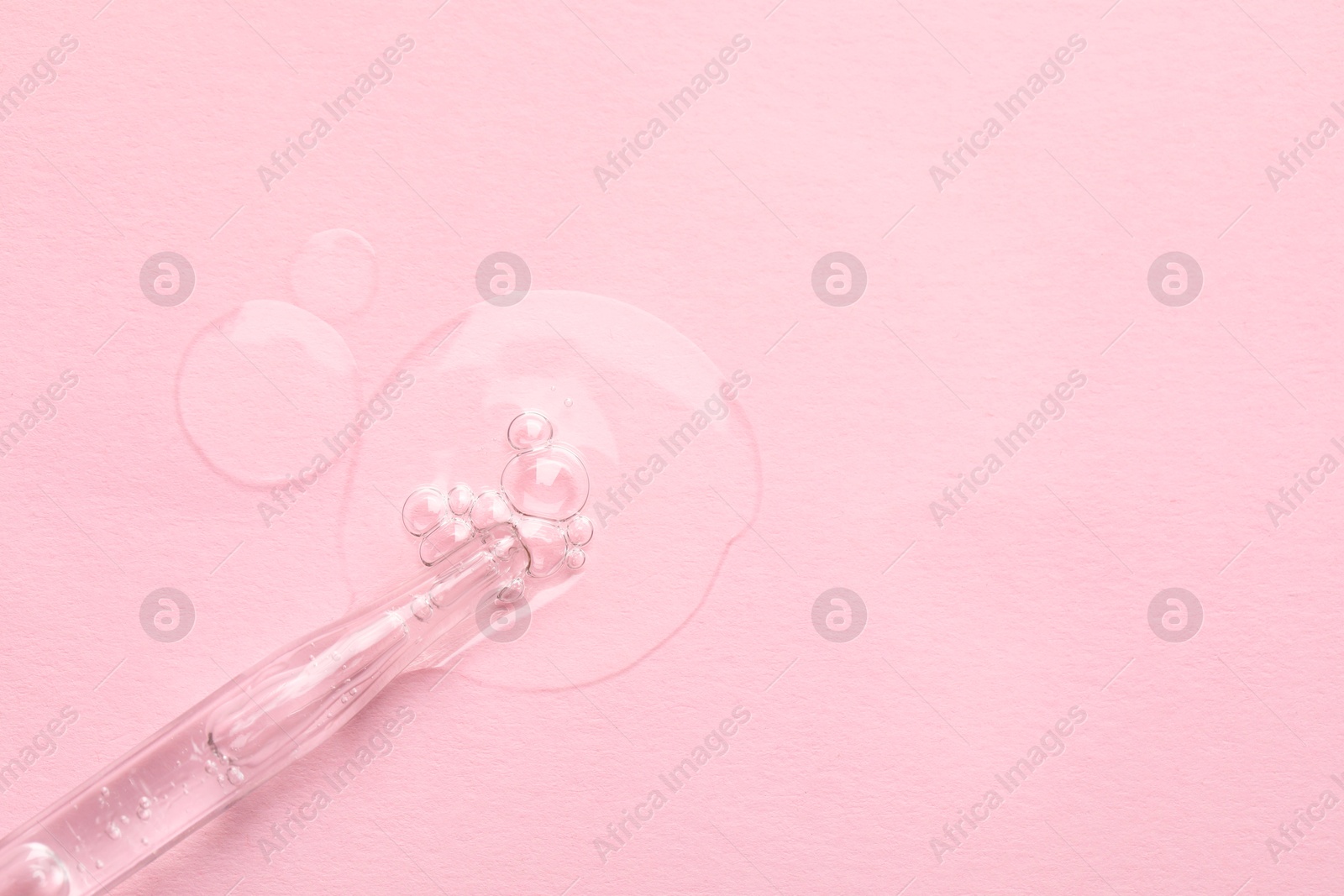 Photo of Glass pipette and transparent liquid on light pink background, top view. Space for text