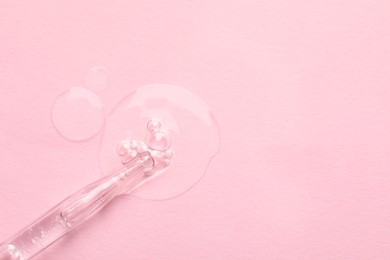 Glass pipette and transparent liquid on light pink background, top view. Space for text