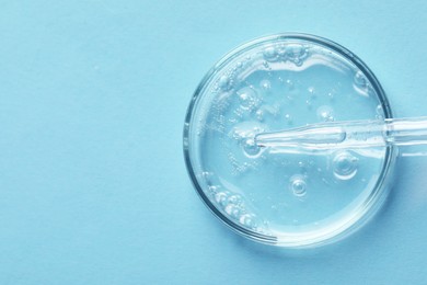 Glass pipette and petri dish with liquid on light blue background, top view. Space for text