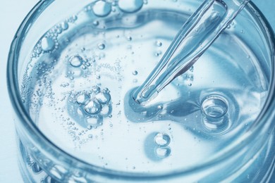 Photo of Glass pipette and petri dish with liquid on light blue background, closeup