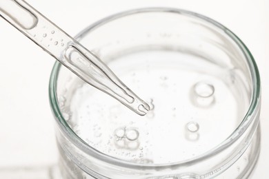 Photo of Glass pipette and petri dish with liquid on beige background, closeup