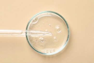 Glass pipette and petri dish with liquid on beige background, top view