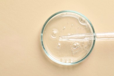 Glass pipette and petri dish with liquid on beige background, top view