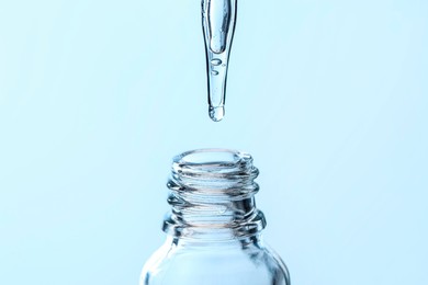 Dripping liquid from pipette into glass bottle on light blue background, closeup