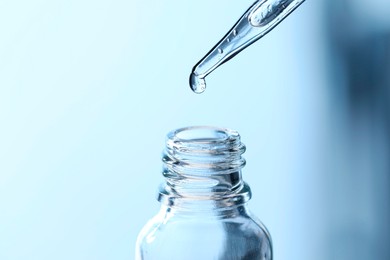 Dripping liquid from pipette into glass bottle on light blue background, closeup