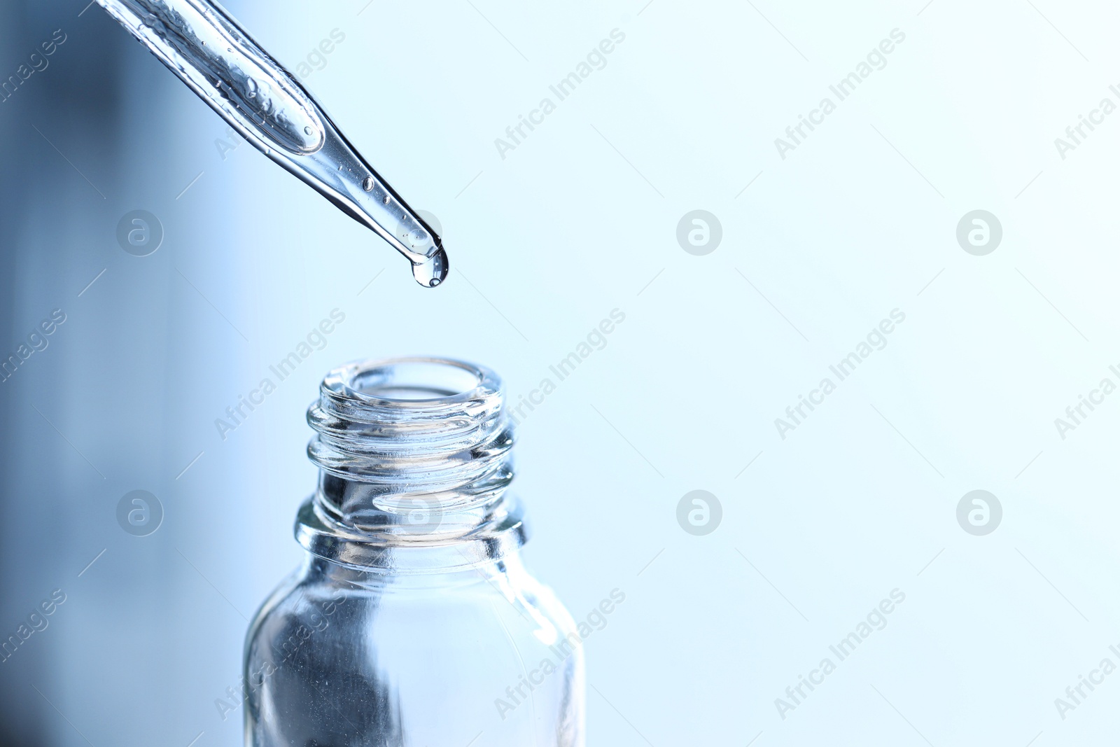 Photo of Dripping liquid from pipette into glass bottle on light blue background, closeup. Space for text