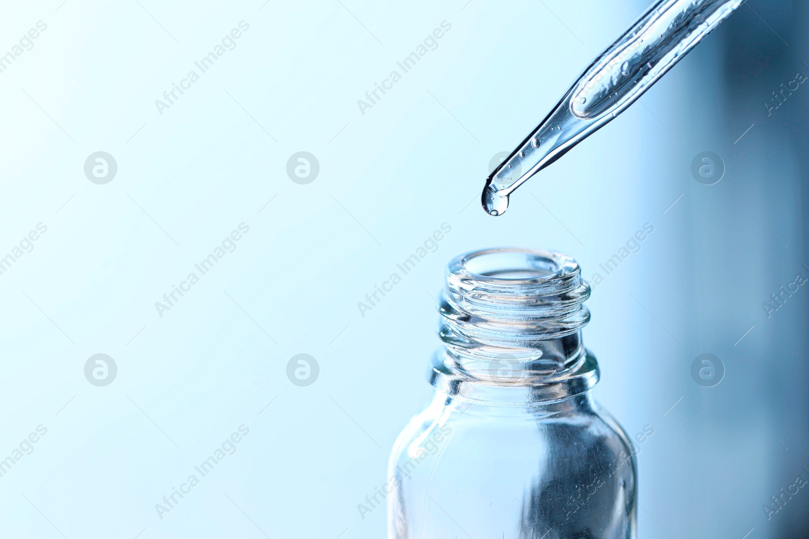 Photo of Dripping liquid from pipette into glass bottle on light blue background, closeup. Space for text