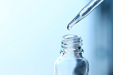Photo of Dripping liquid from pipette into glass bottle on light blue background, closeup. Space for text