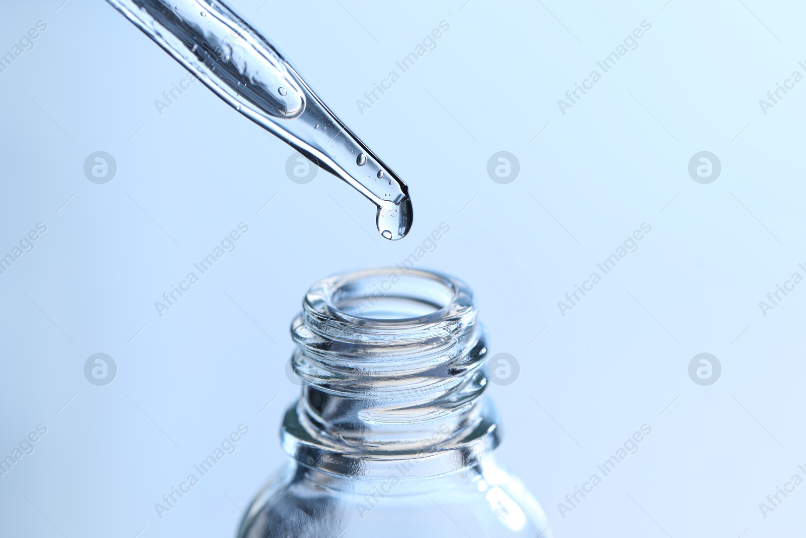 Photo of Dripping liquid from pipette into glass bottle on light blue background, closeup