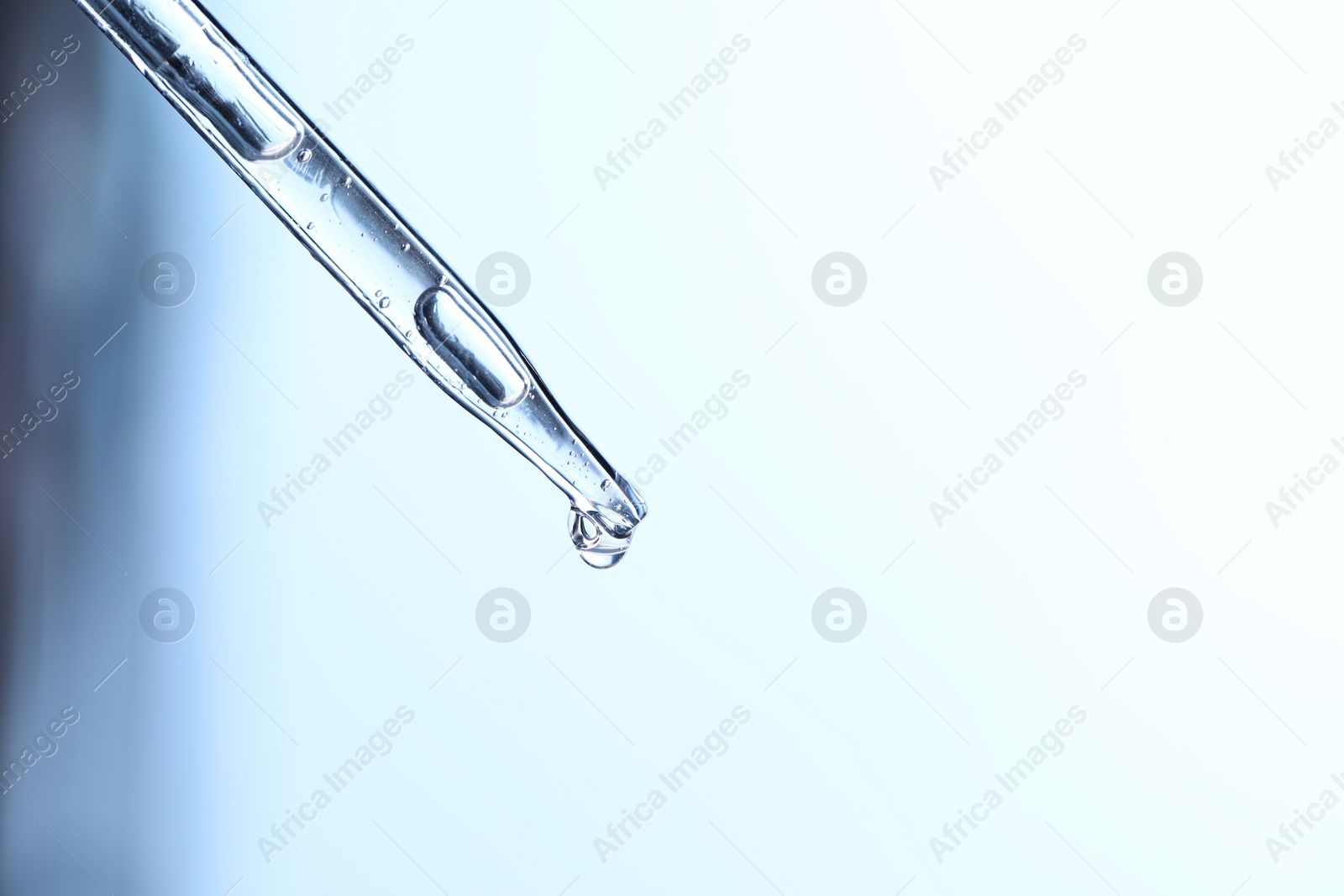 Photo of Dripping liquid from pipette on light blue background, closeup. Space for text