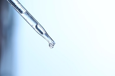 Dripping liquid from pipette on light blue background, closeup. Space for text