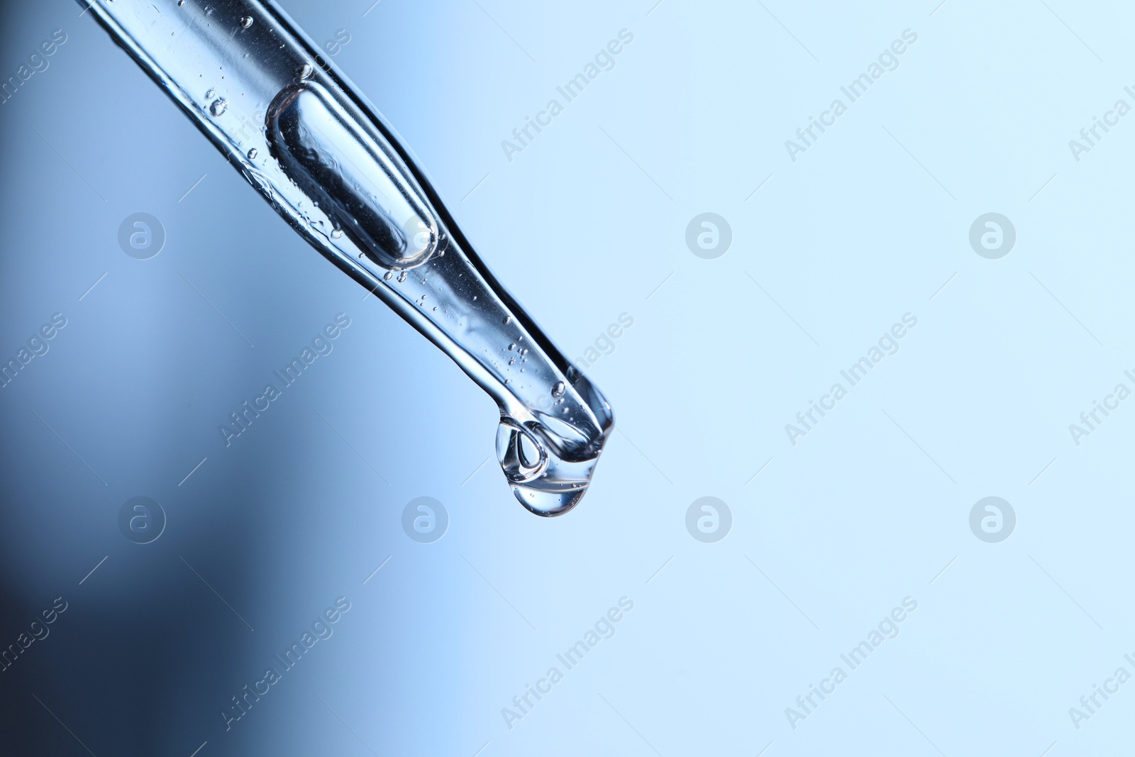 Photo of Dripping liquid from pipette on light blue background, closeup