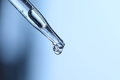 Dripping liquid from pipette on light blue background, closeup