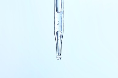 Photo of Dripping liquid from pipette on light blue background, closeup