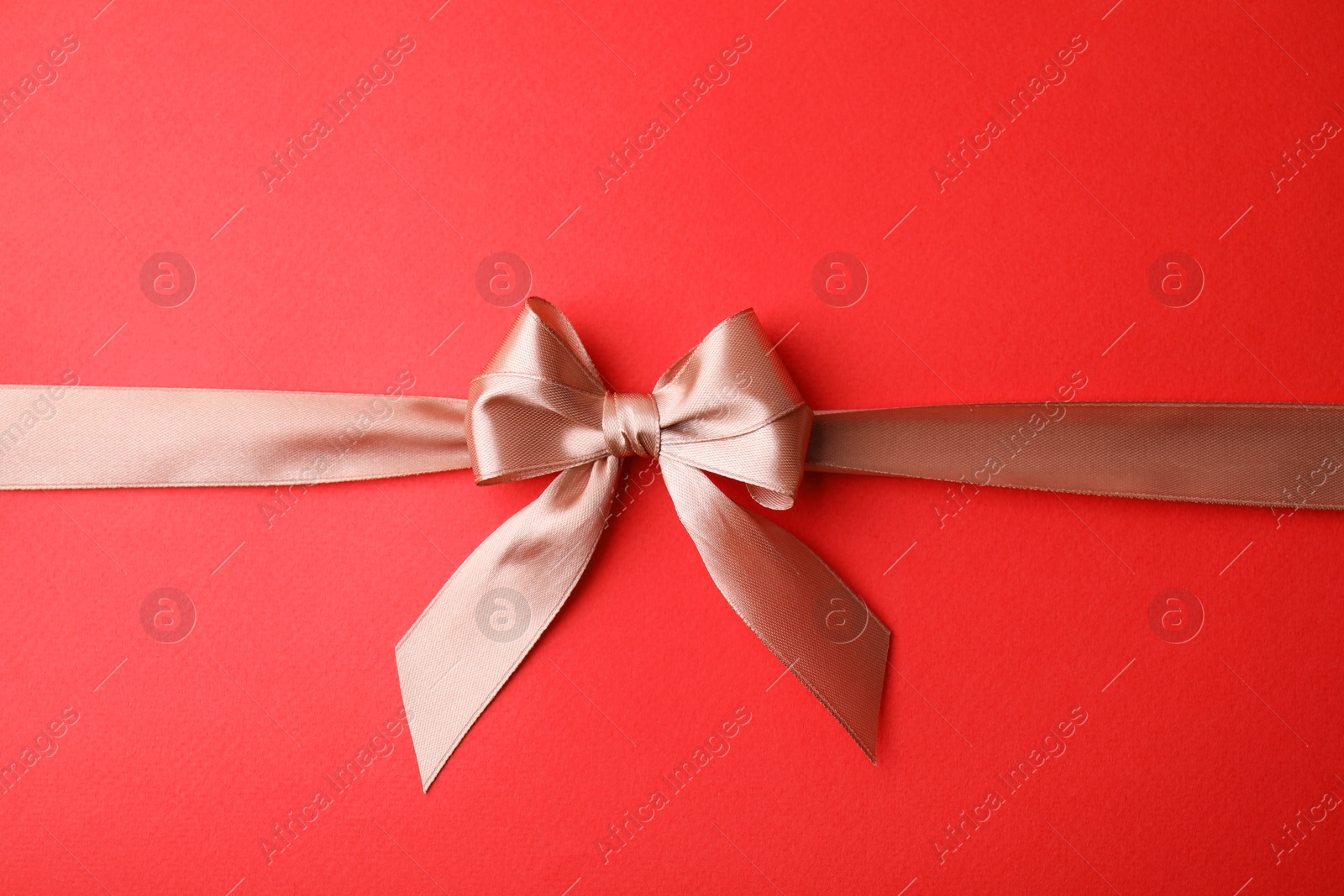 Photo of Beige satin ribbon with bow on red background, top view