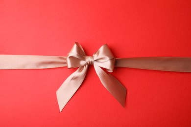 Beige satin ribbon with bow on red background, top view