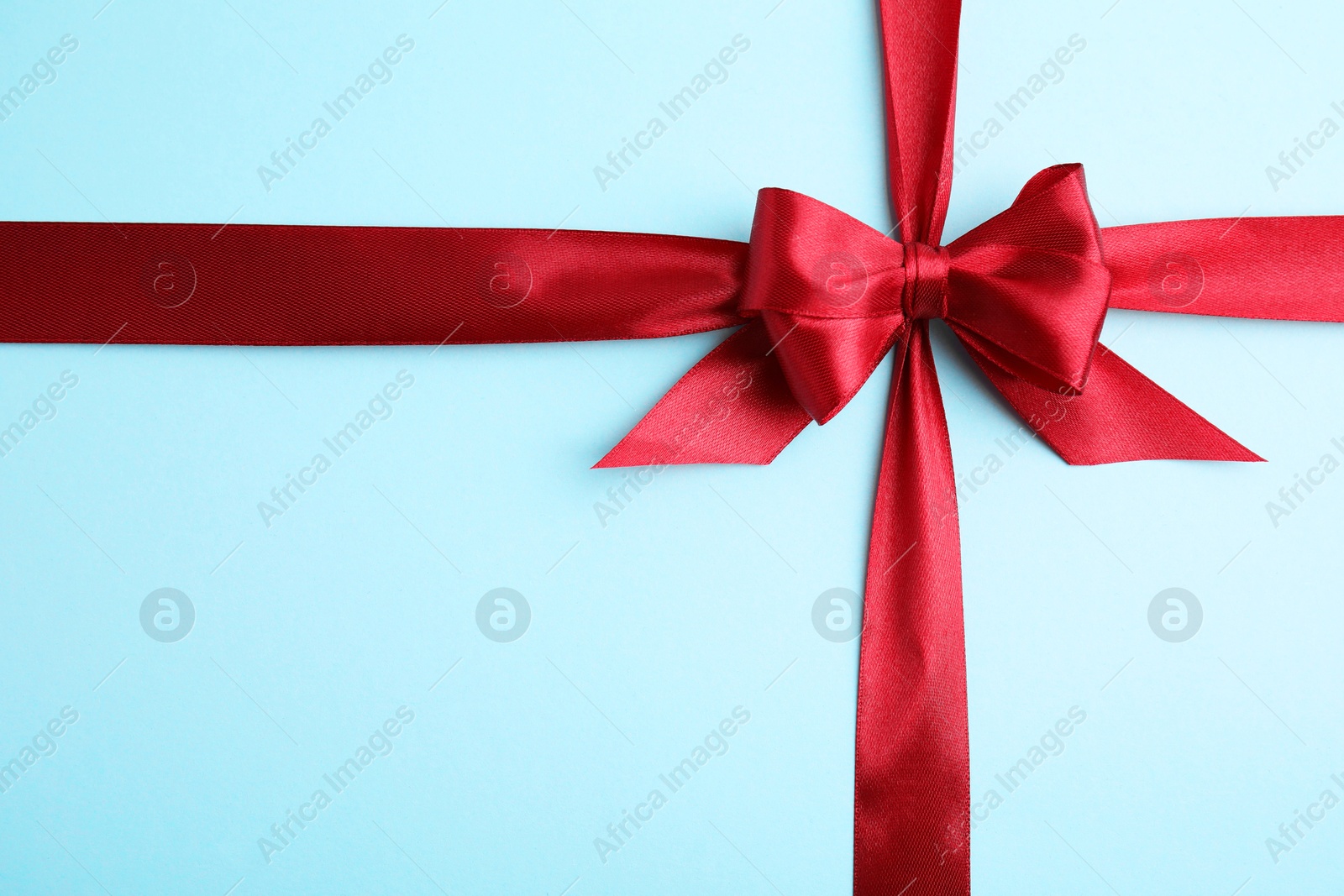 Photo of Red satin ribbon with bow on light blue background, top view