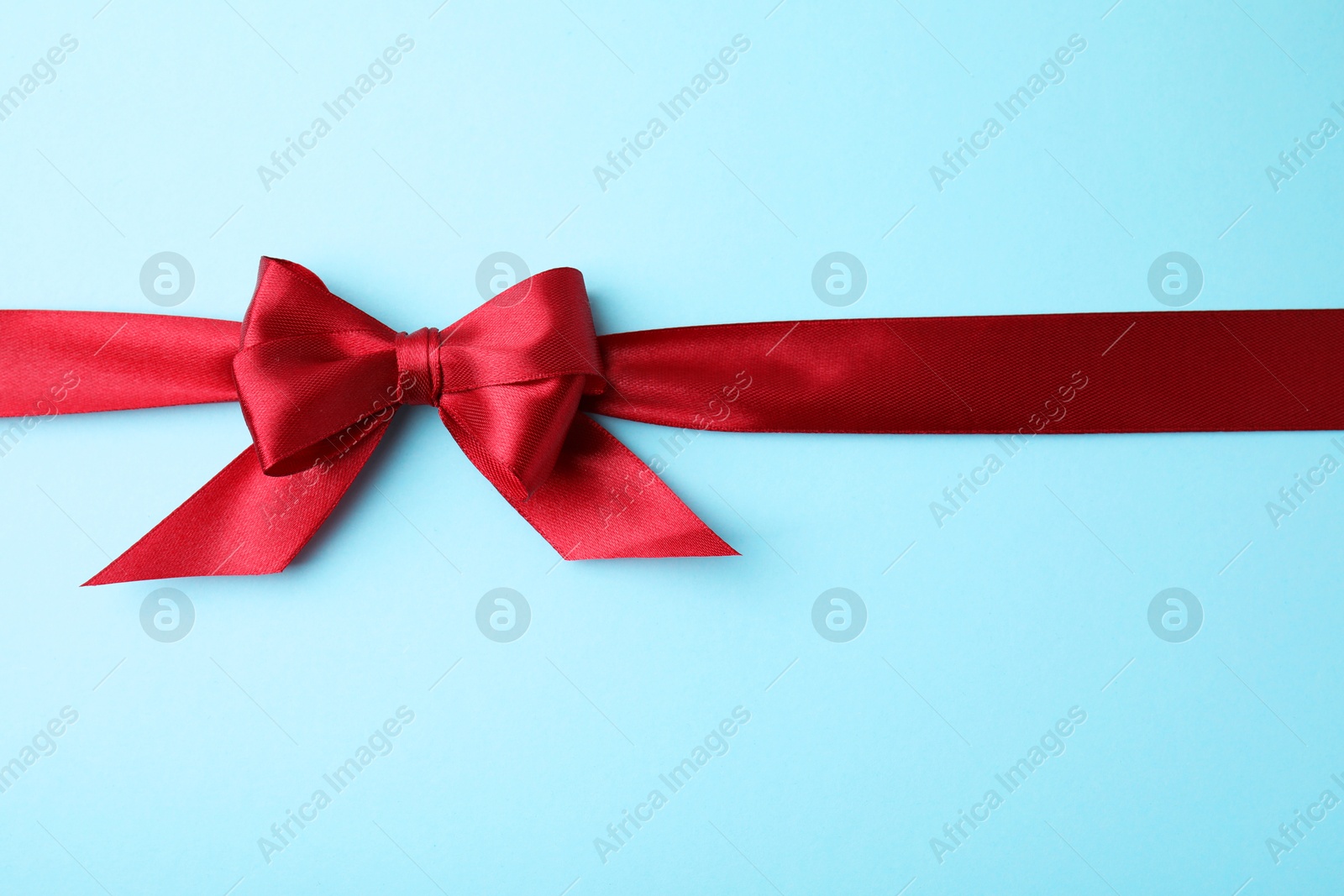 Photo of Red satin ribbon with bow on light blue background, top view