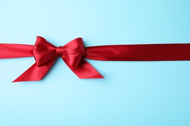 Red satin ribbon with bow on light blue background, top view