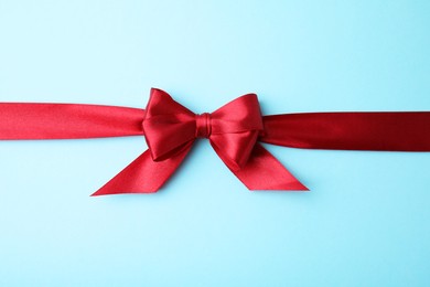 Red satin ribbon with bow on light blue background, top view