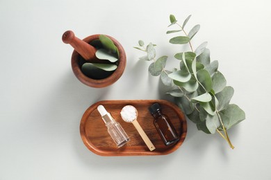 Different aromatherapy products, mortar and eucalyptus branches on grey background, flat lay