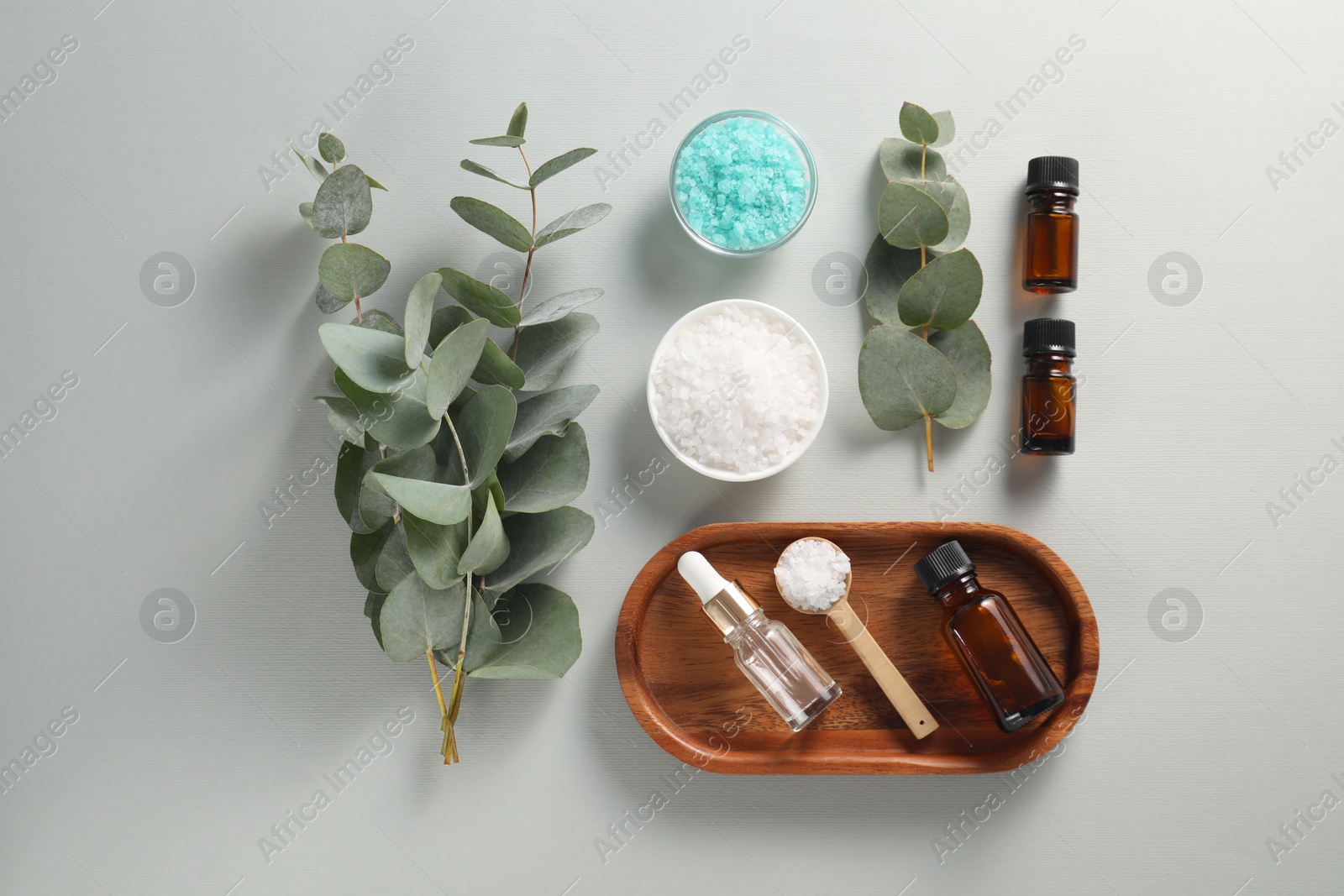 Photo of Aromatherapy products. Bottles of essential oil, sea salt and eucalyptus branches on grey background, flat lay