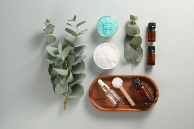 Photo of Aromatherapy products. Bottles of essential oil, sea salt and eucalyptus branches on grey background, flat lay