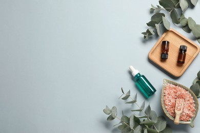 Photo of Aromatherapy products. Bottles of essential oil, sea salt and eucalyptus branches on grey background, flat lay. Space for text