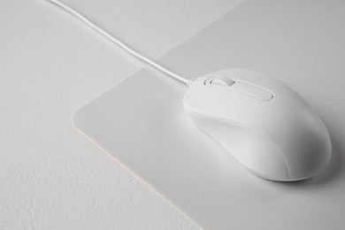 Photo of Wired mouse with mousepad on light textured table, closeup