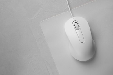 Photo of Wired mouse with mousepad on grey textured table, top view. Space for text