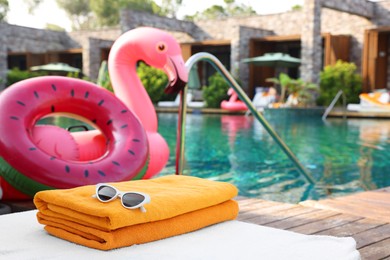 Beach accessories on sun lounger, inflatable ring and float near outdoor swimming pool at luxury resort, space for text