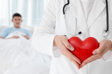 Doctor holding red heart in clinic, selective focus