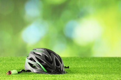 Photo of Stylish protective helmet on green grass against blurred background. Space for text