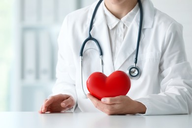 Photo of Doctor with red heart at table in clinic, closeup