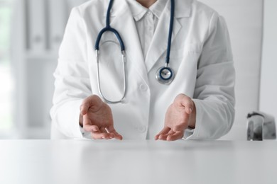 Photo of Doctor with stethoscope holding something at table in clinic, closeup