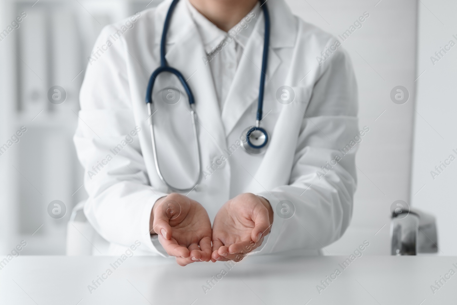 Photo of Doctor with stethoscope holding something at table in clinic, closeup