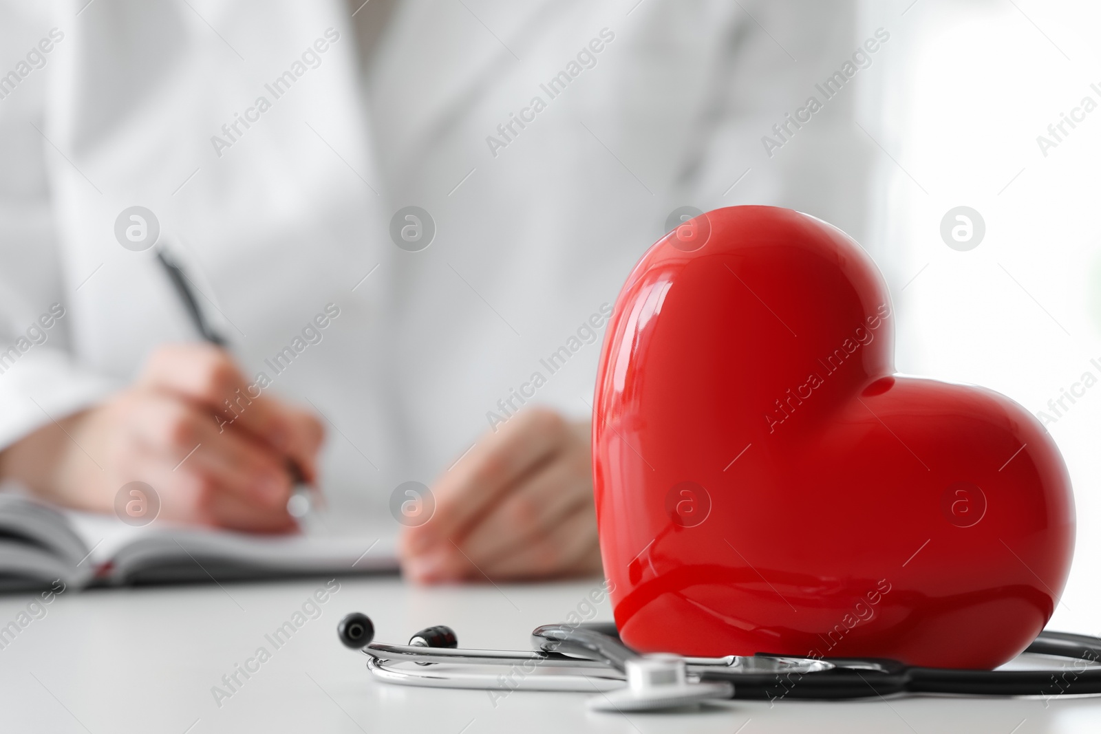 Photo of Doctor working at table in clinic, focus on red heart