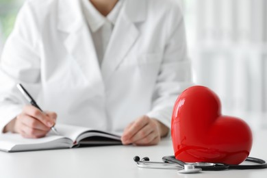 Photo of Doctor working at table in clinic, focus on red heart
